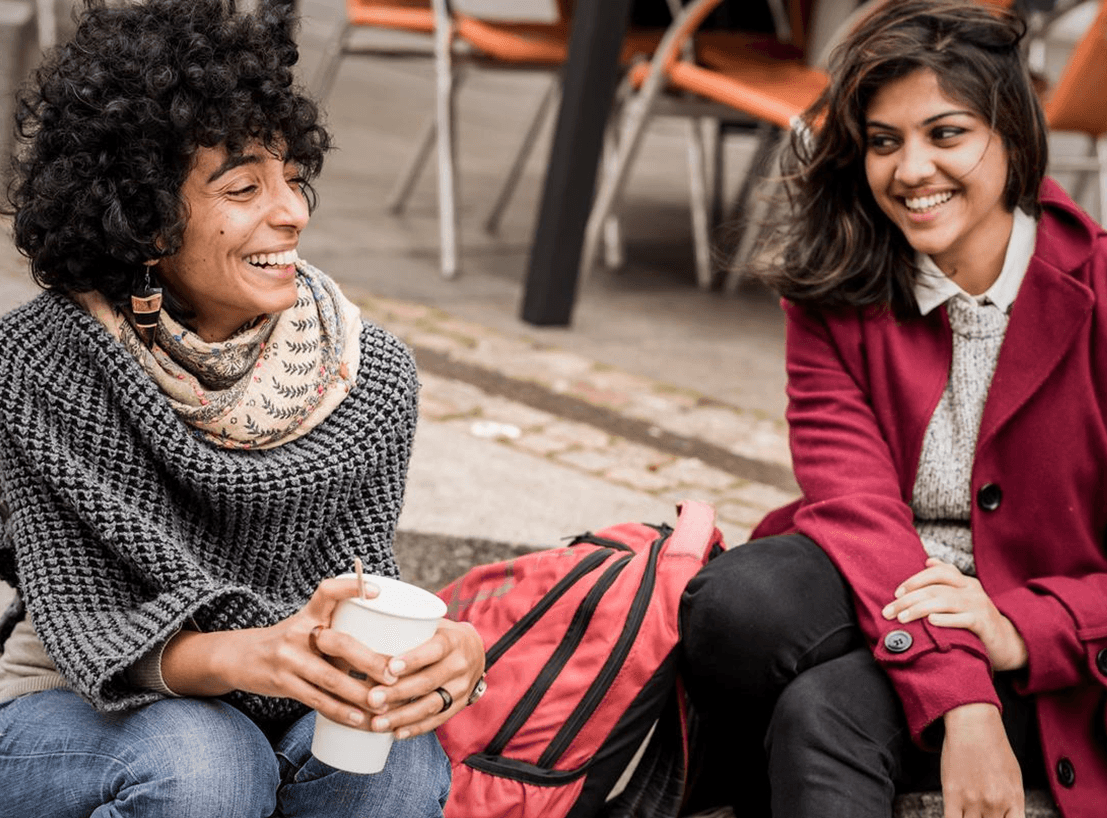to kvinder griner sammen og drikker kaffe, udendørs
